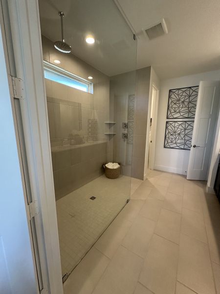 A spacious shower with sleek glass doors and modern beige tiles, featuring elegant artwork on the wall.