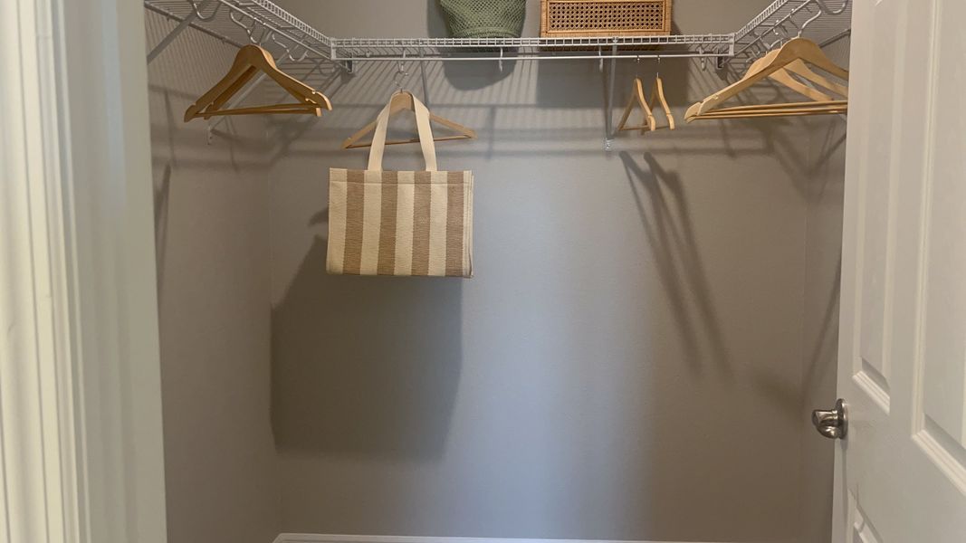 A spacious walk-in closet featuring wire shelving, wooden hangers, and a stylish woven bag for organized elegance.