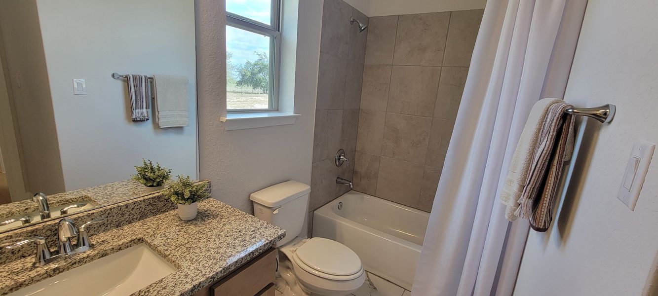 A modern bathroom featuring a granite countertop, sleek fixtures, and a tiled shower area with a fresh, neutral palette.