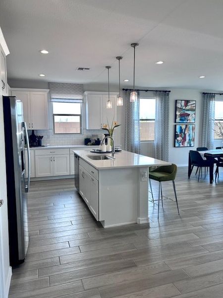 A modern kitchen with sleek white cabinets, an island, stainless steel appliances, and elegant pendant lighting.