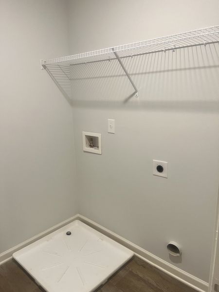 A functional laundry space with tile flooring, wall shelving, and utility connections ready for appliances.