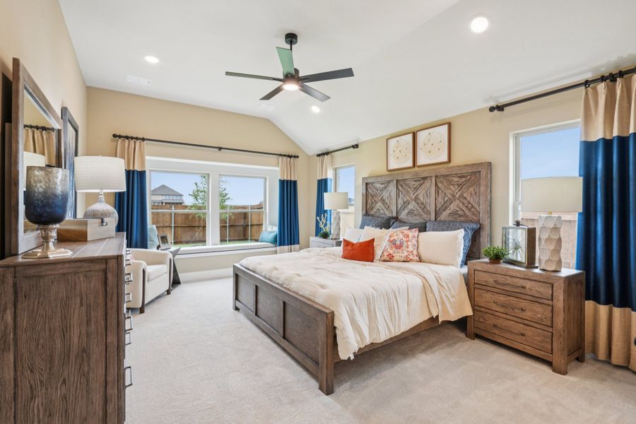 Master bedroom with vaulted ceiling, wood bed frame, ceiling fan, and large windows with blue curtains Master bedroom with vaulted ceiling, wood bed frame, ceiling fan, and large windows with blue curtains