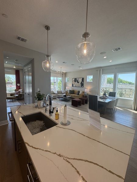 A modern open-concept living area with a sleek kitchen island, pendant lighting, and bright, airy dining space.