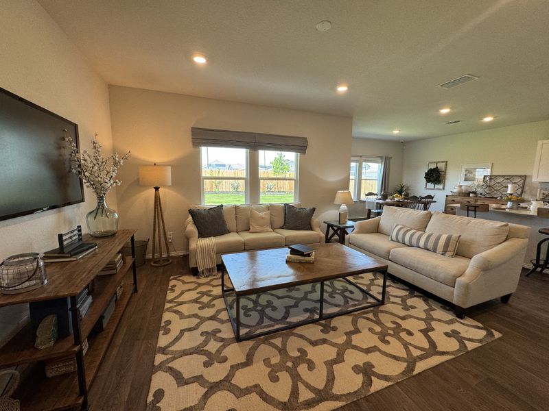 A cozy living room featuring plush seating, a patterned rug, and warm lighting, with views of a bright kitchen beyond.