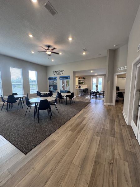 A spacious community room with modern flooring, round tables, and bright lighting creates an inviting atmosphere.