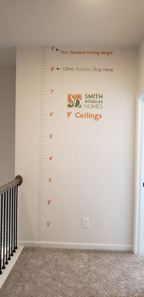 A wall showcasing a height comparison with 9' standard ceilings by Smith Douglas Homes, featuring a carpeted floor. A wall showcasing a height comparison with 9' standard ceilings by Smith Douglas Homes, featuring a carpeted floor.