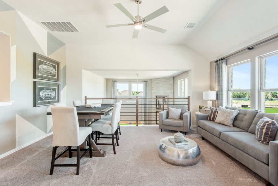 Upstairs loft with vaulted ceiling, ceiling fan, gray seating area, and game table near open railing Upstairs loft with vaulted ceiling, ceiling fan, gray seating area, and game table near open railing