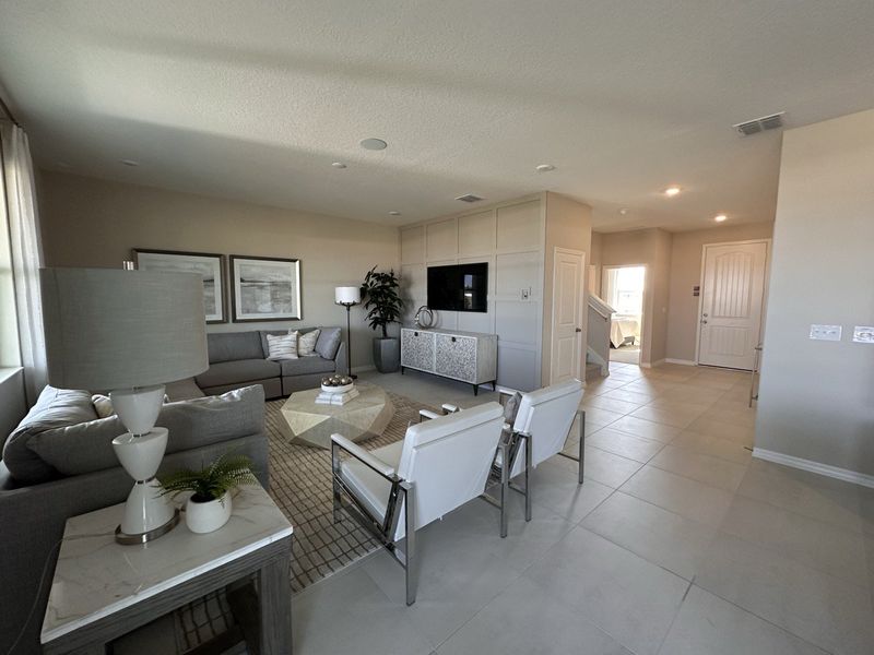 A bright living room with neutral décor, a sectional sofa, and contemporary accents in Landings at Lake Mabel Loop by KB Home (Dundee, FL).