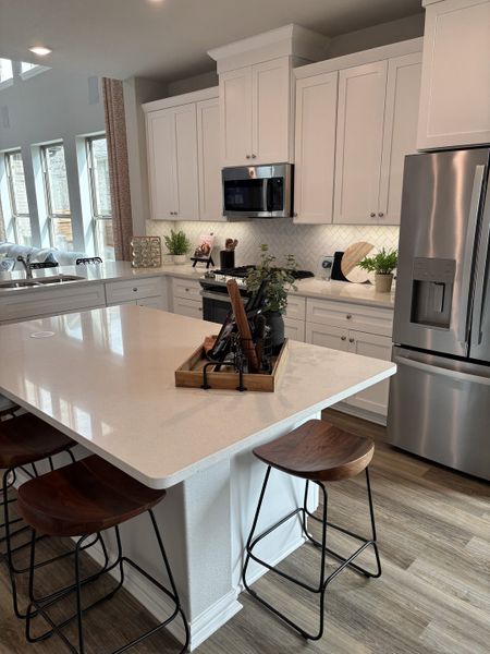 A modern kitchen with sleek white cabinetry, a spacious island, wooden stools, and elegant lighting accents. A modern kitchen with sleek white cabinetry, a spacious island, wooden stools, and elegant lighting accents.