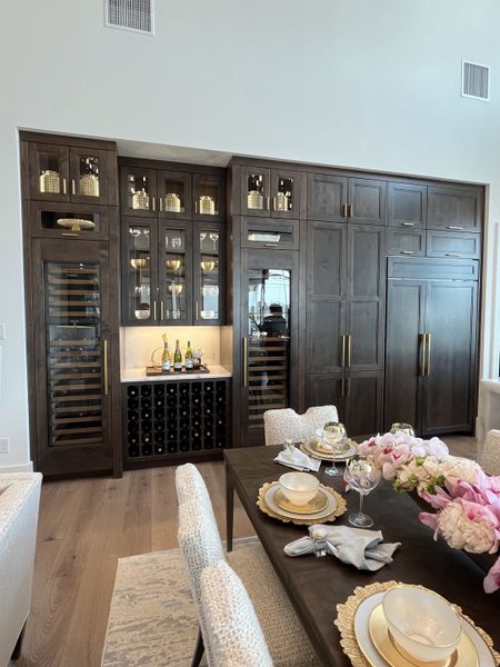 Elegant dining area featuring dark wood cabinetry, integrated wine fridge, and a sophisticated table setting with pink florals.