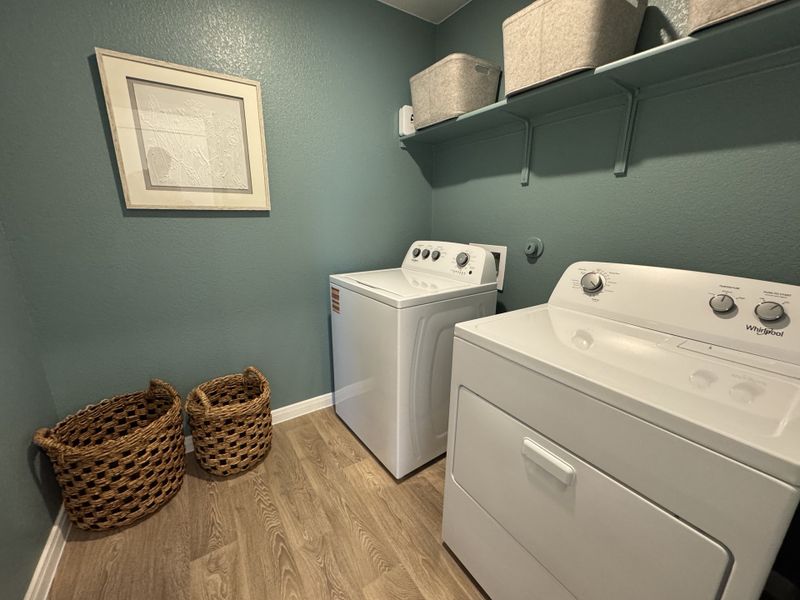A cozy laundry room with teal walls, modern washer and dryer, wicker baskets, and minimalist shelving for storage. A cozy laundry room with teal walls, modern washer and dryer, wicker baskets, and minimalist shelving for storage.