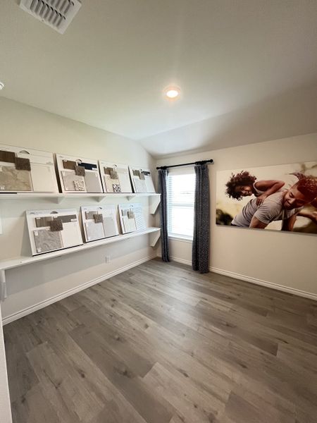A cozy room with wood flooring, open shelving displaying design materials, and a large window draped with elegant curtains.