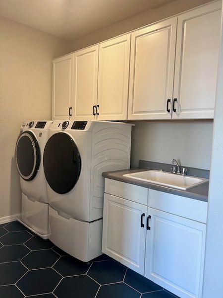 A sleek laundry room with modern appliances, white cabinetry, and a convenient sink on a stylish dark hexagon tile floor. A sleek laundry room with modern appliances, white cabinetry, and a convenient sink on a stylish dark hexagon tile floor.