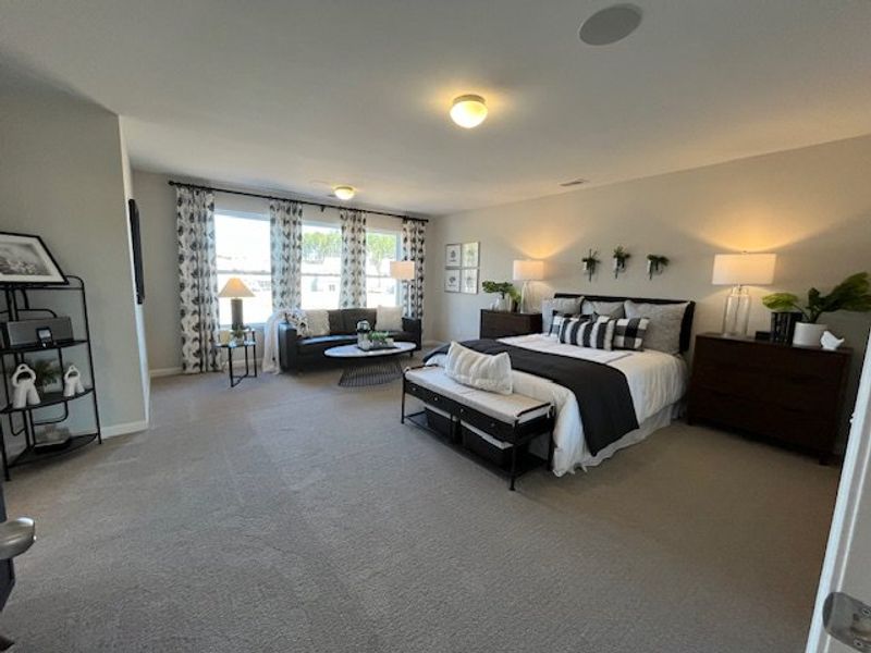Spacious bedroom featuring cozy seating, plush bedding, and abundant natural light with stylish decor elements.
