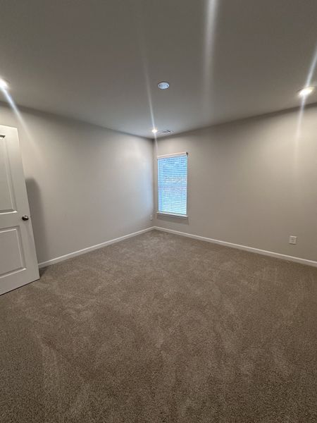 A cozy, carpeted room with neutral walls, recessed lighting, and a small window, perfect for a home office or guest room.