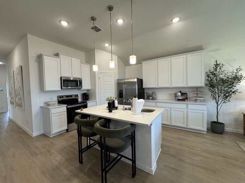 A modern kitchen featuring white cabinetry, a central island with seating, and sleek appliances. Bright and open with stylish lighting.