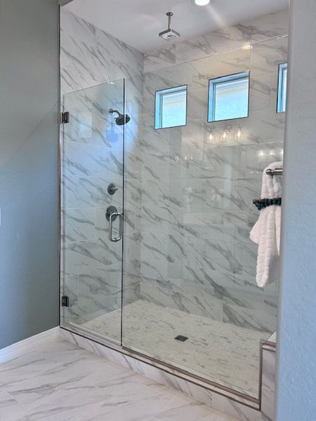 Elegant glass-enclosed shower with marble-patterned tiles and sleek fixtures.