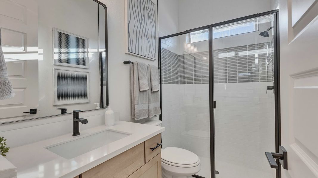 Elegant bathroom features a frameless glass shower, sleek black fixtures, and a luxurious wood vanity in Creeks Crossing.