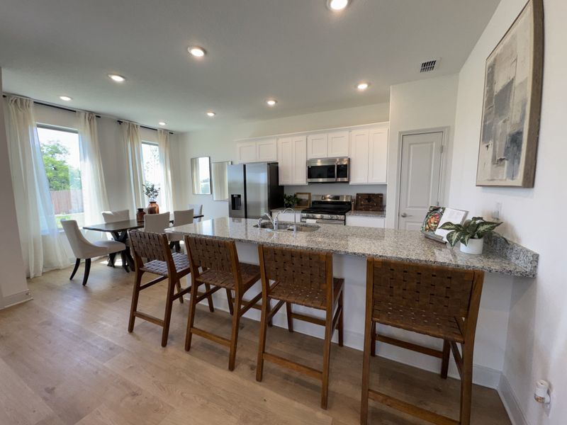 An open kitchen with a granite island, sleek appliances, and a cozy dining area set against large, bright windows. An open kitchen with a granite island, sleek appliances, and a cozy dining area set against large, bright windows.