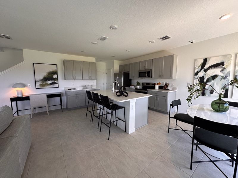 A modern kitchen with gray cabinets, a central island, sleek appliances, and stylish artwork, featuring an open dining area.