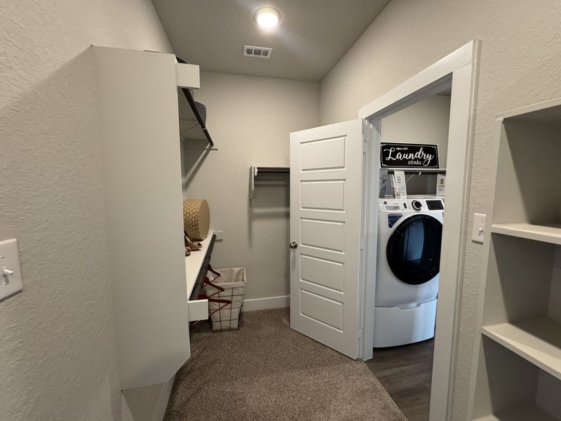 A functional laundry room with modern washer/dryer, open shelving, and cozy carpeted floor. A functional laundry room with modern washer/dryer, open shelving, and cozy carpeted floor.