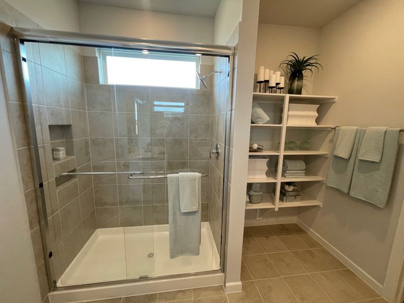 A modern bathroom featuring a tiled shower, sleek glass door, and organized shelving with towels and décor accents.