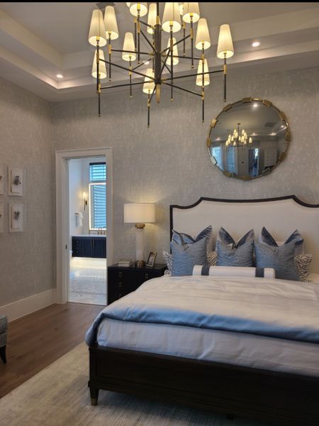 Elegant bedroom with a modern chandelier, plush bedding, and chic wall mirror for a luxurious retreat.