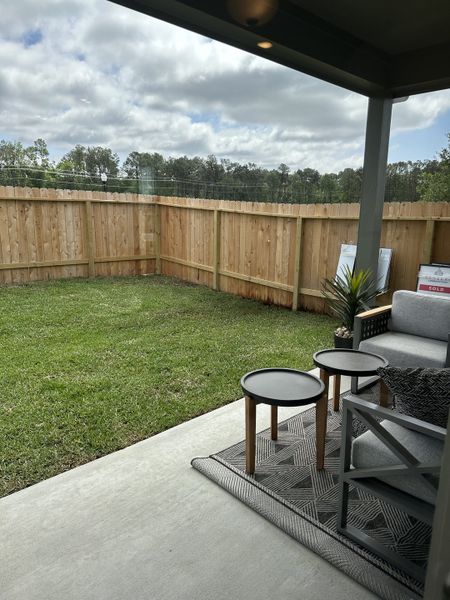 A cozy covered patio with stylish outdoor seating, overlooking a private fenced yard.