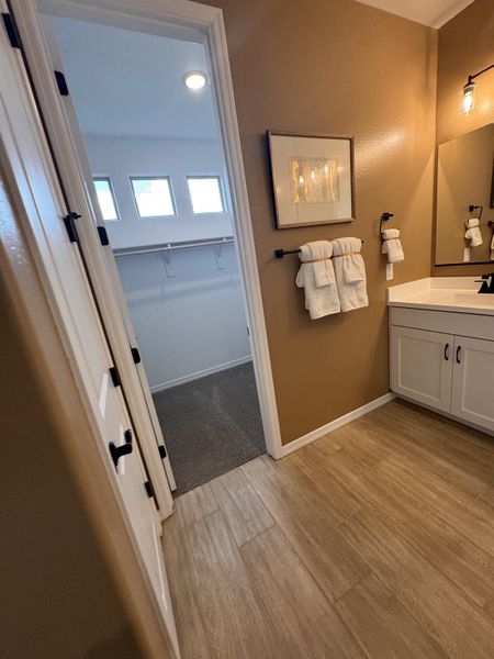 A warm bathroom with wood-look tile, white vanity, and entry to a walk-in closet with natural light.
