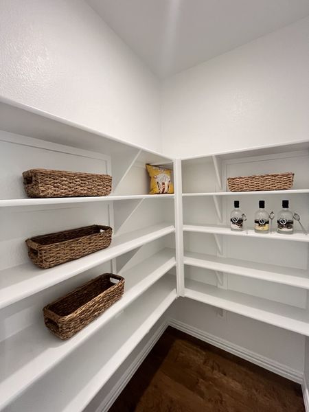 A spacious pantry with white shelving, wicker baskets for organization, and a neatly arranged wooden floor.