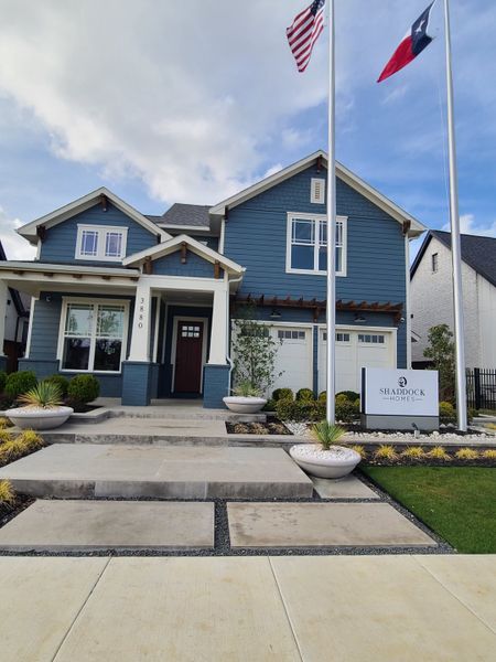 A charming blue home with a welcoming porch and manicured landscaping in Fields - 50' Lots by Shaddock Homes (Frisco, TX).