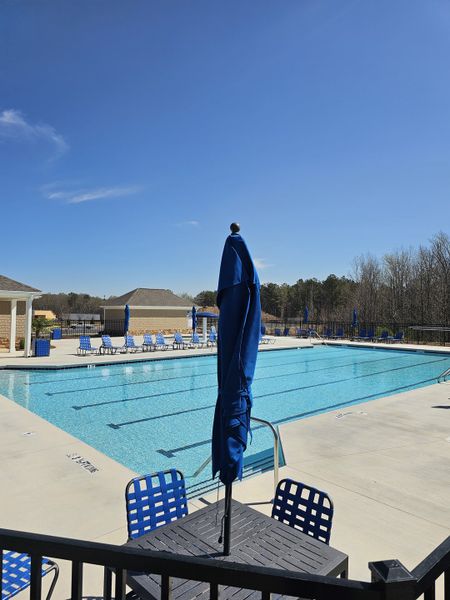 A luxurious pool area with blue lounge chairs and umbrellas in Braselton Village by D.R. Horton (Braselton, GA).