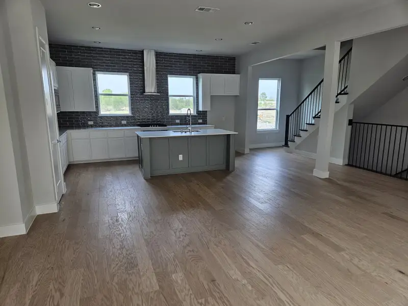 A spacious kitchen with a central island, dark textured backsplash, light wood floors, and ample natural light.