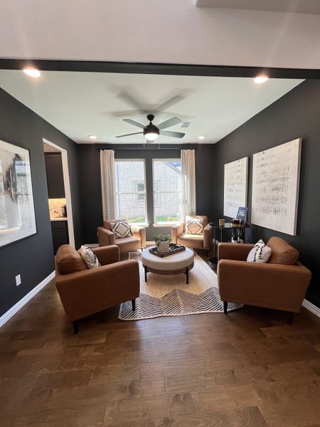 A cozy living area with warm wood floors, stylish armchairs, and modern decor in a sleek, dark-painted room.