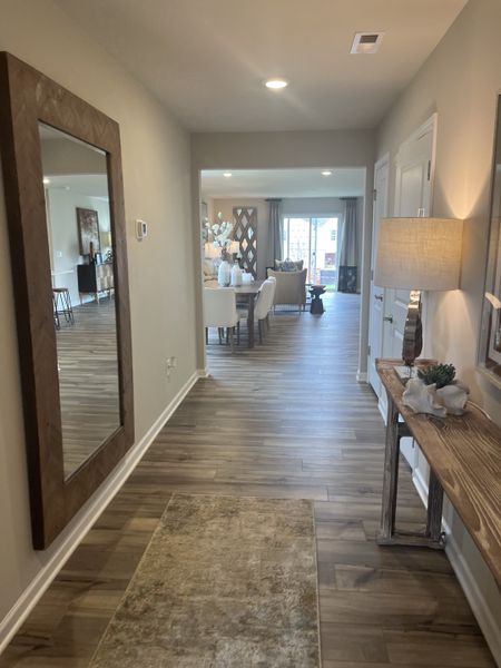 A welcoming hallway leading to a bright living area with wood flooring, elegant decor, and large windows. A welcoming hallway leading to a bright living area with wood flooring, elegant decor, and large windows.