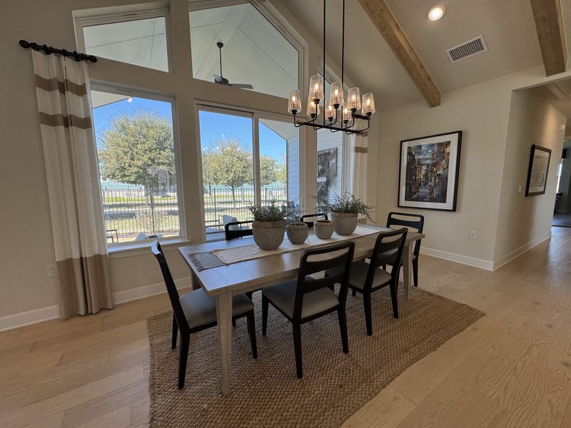 A bright dining room with large windows, a modern chandelier, and natural decor on wooden floors.