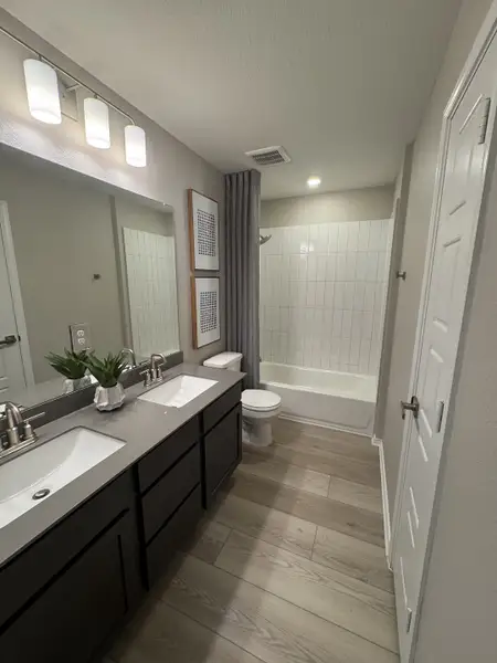 A modern bathroom featuring a sleek double sink, stylish faucet, wood flooring, and bright lighting. A modern bathroom featuring a sleek double sink, stylish faucet, wood flooring, and bright lighting.