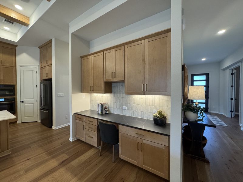 A modern kitchen with sleek wooden cabinets, a built-in desk, and bright lighting, offering both functionality and style.