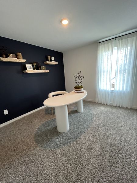 A contemporary home office with a navy accent wall, floating shelves, and a unique oval desk on plush carpet.