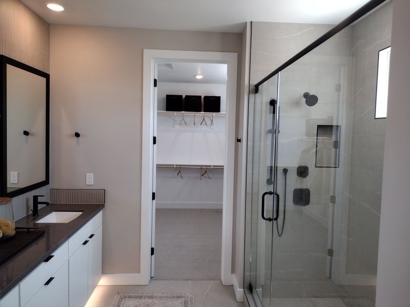 A modern bathroom with a glass shower, sleek black vanity, and LED lighting, leading to a walk-in closet. A modern bathroom with a glass shower, sleek black vanity, and LED lighting, leading to a walk-in closet.