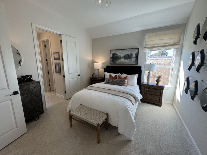 A cozy bedroom featuring neutral decor, plush bedding, and natural light filtering through a window with tasteful accessories.