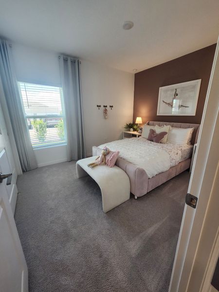 A cozy bedroom with soft carpeting, a plush bed, accent wall, and elegant drapes. Perfectly inviting and stylish.