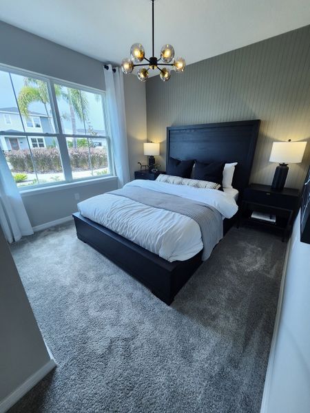 A cozy bedroom with a modern chandelier, plush carpeting, and large windows offering natural light. A cozy bedroom with a modern chandelier, plush carpeting, and large windows offering natural light.