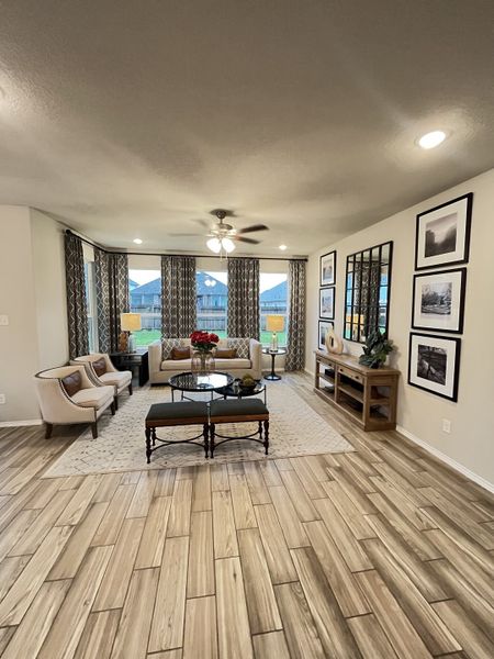 A cozy living room with wood-style flooring, elegant seating, and large windows framed by patterned drapes.