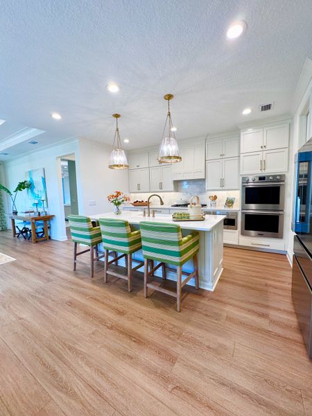 A bright kitchen featuring white cabinetry, green striped chairs, pendant lighting, and sleek hardwood flooring.