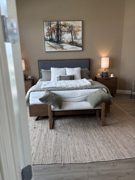 A cozy bedroom with modern bedding, textured rug, ambient lighting, and serene landscape artwork on the wall. A cozy bedroom with modern bedding, textured rug, ambient lighting, and serene landscape artwork on the wall.