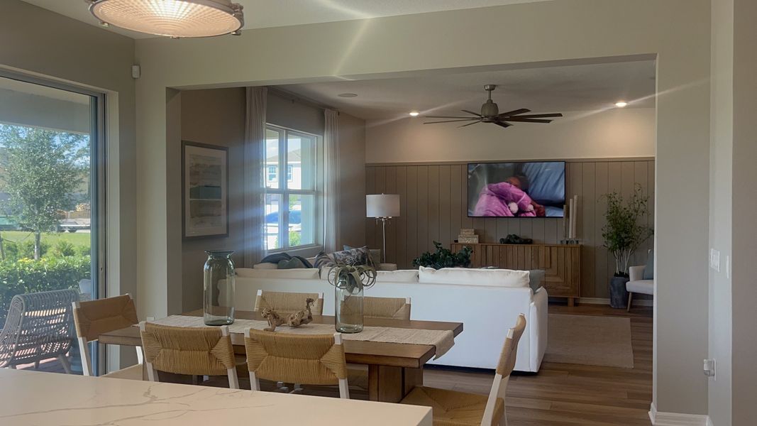 A cozy living room with a plush white sofa, wooden dining set, large windows, and modern decor.