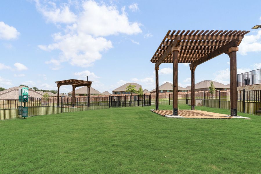 Fenced dog park with green grass, two wooden pergolas, and waste station in a residential community
