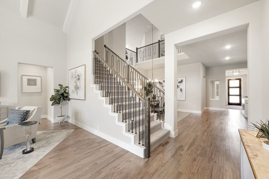 Two-story foyer with carpeted staircase, iron balusters, hardwood floors, and open hallway leading to front door