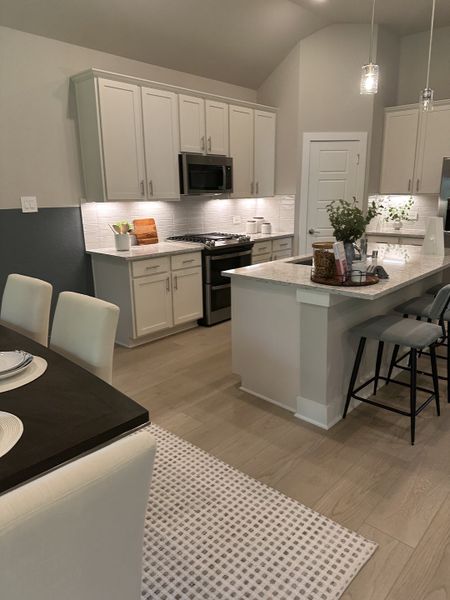 Modern kitchen with sleek cabinets, island seating, and elegant lighting. Dining area features a cozy rug and stylish table.